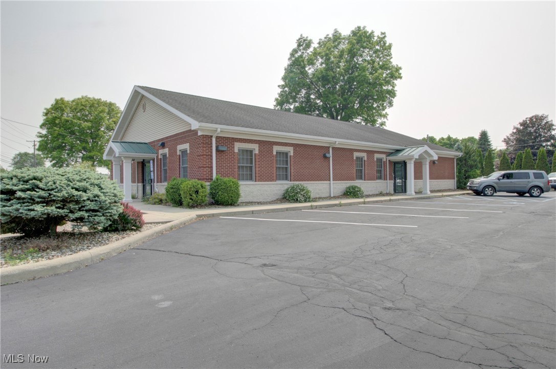Red brick commercial building with white trim and columns in a parking lot setting.