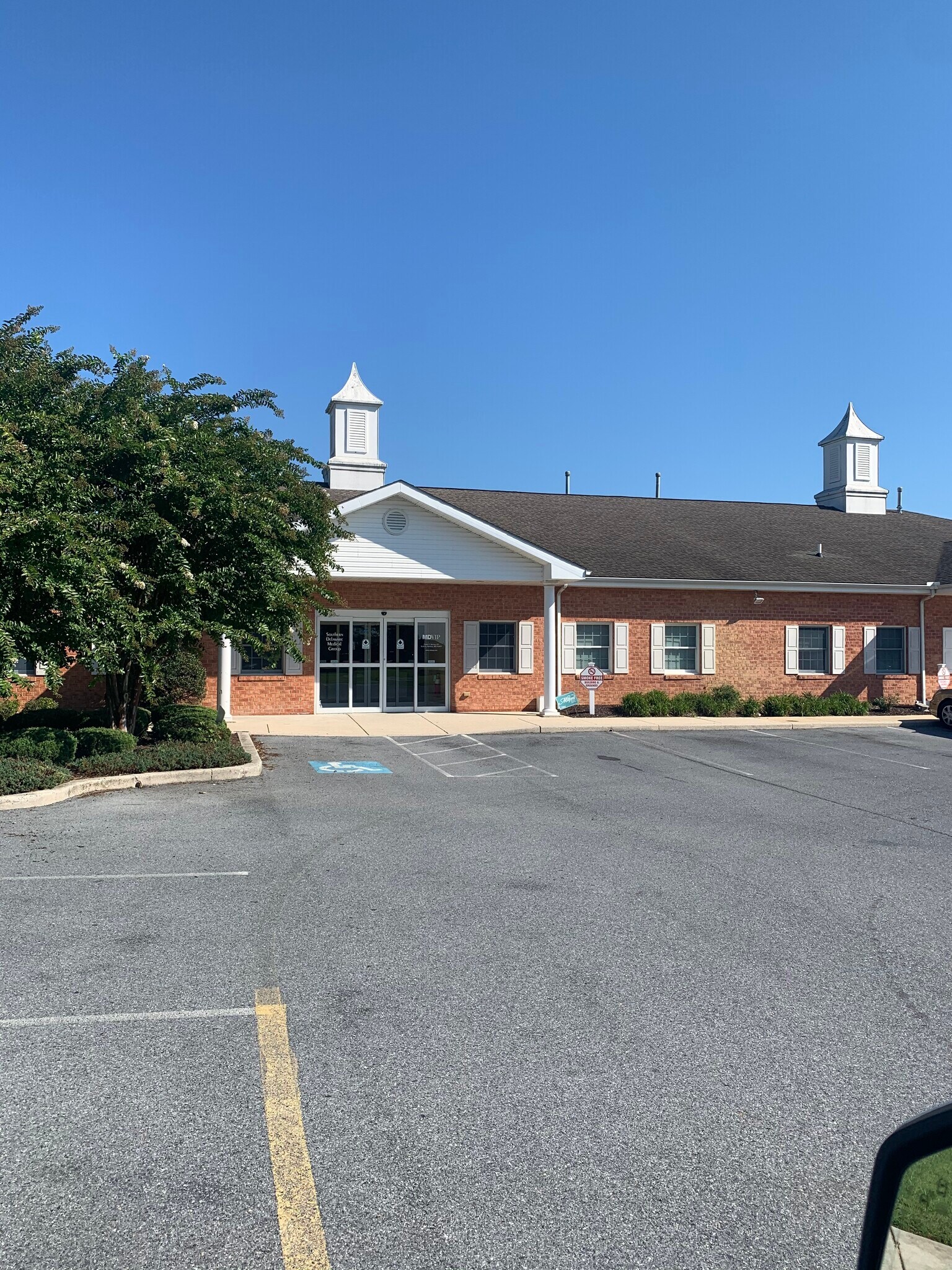 Red brick church building with white steeples under clear blue sky in a parking lot.