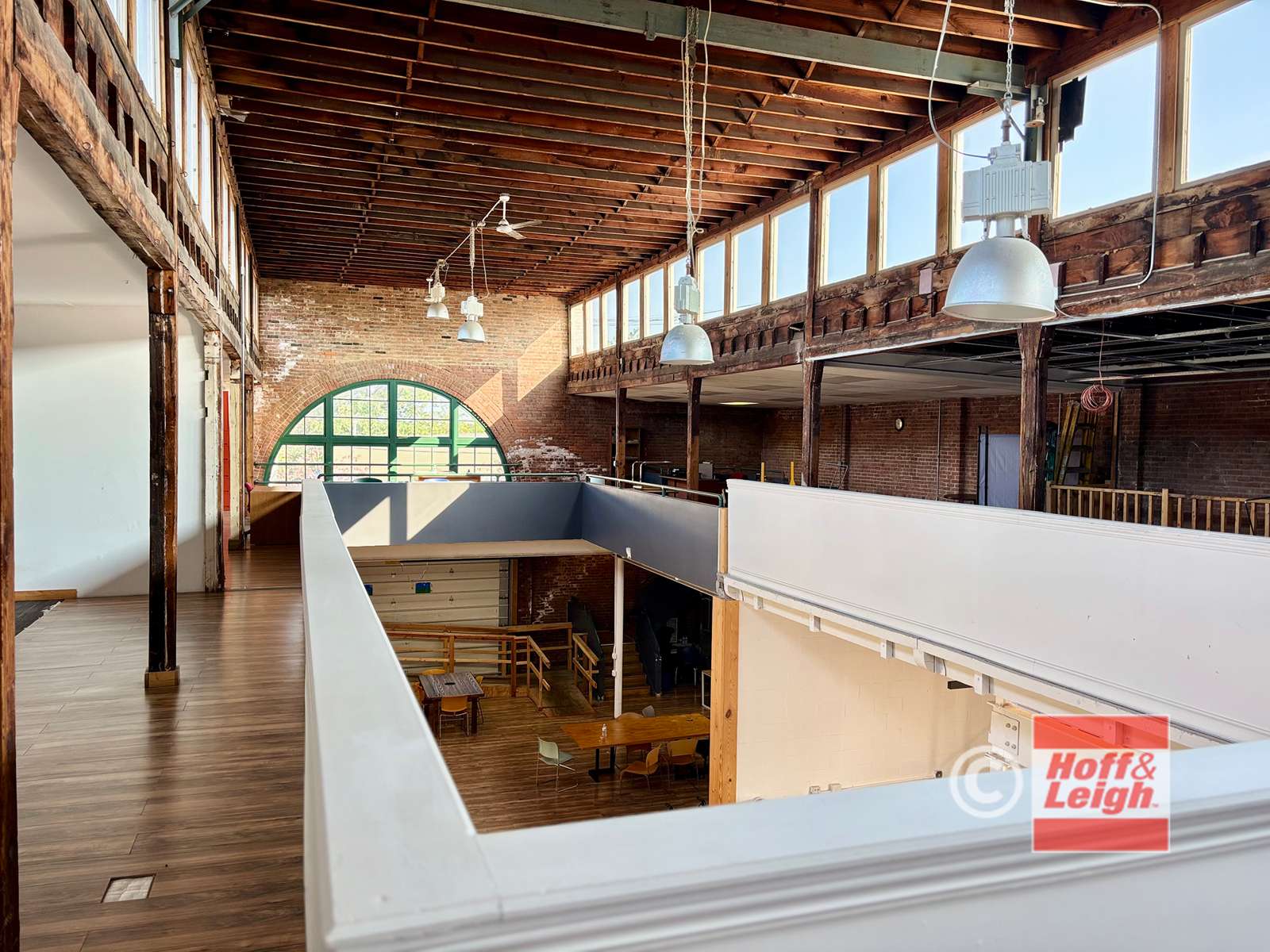 Modern loft interior with exposed brick, wooden beams, pendant lighting, and multi-level white railings overlooking lower floor space.