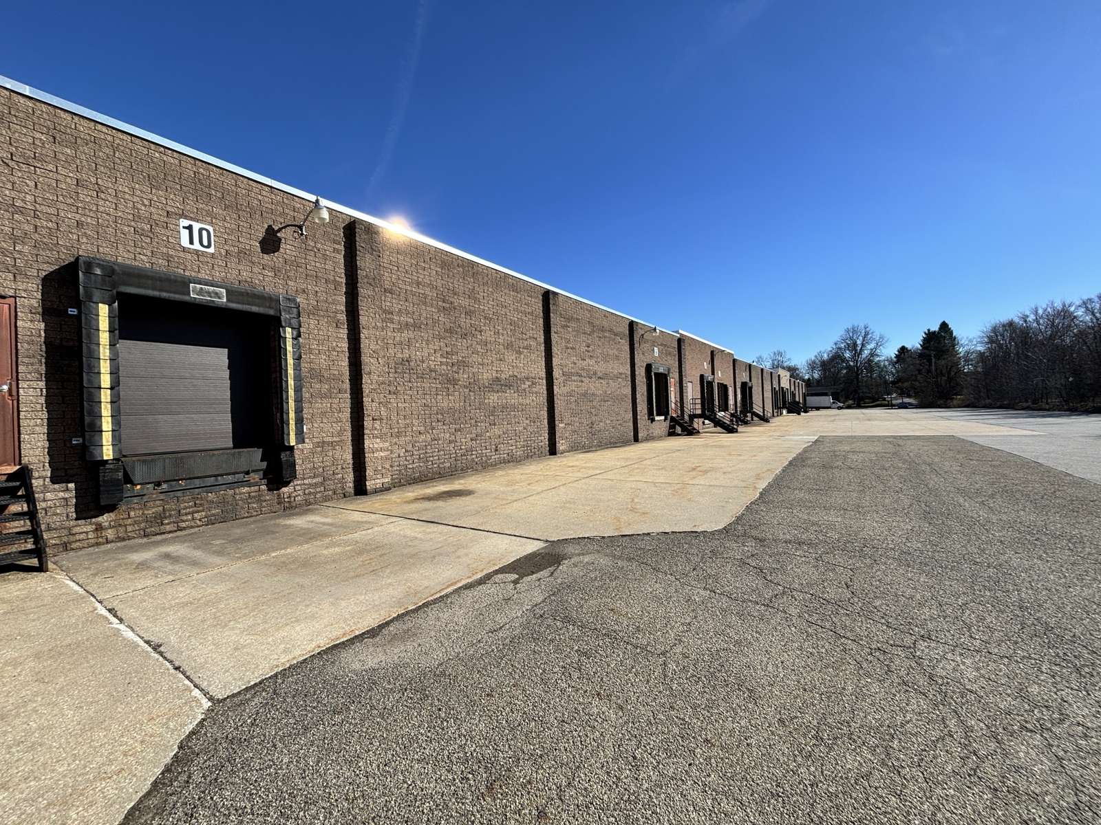 Industrial warehouse building with multiple loading dock doors along brick facade and asphalt parking area.