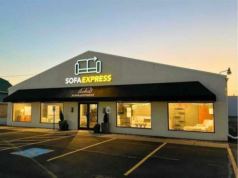 Sofa Express storefront at dusk with illuminated windows and black awning in a parking lot.