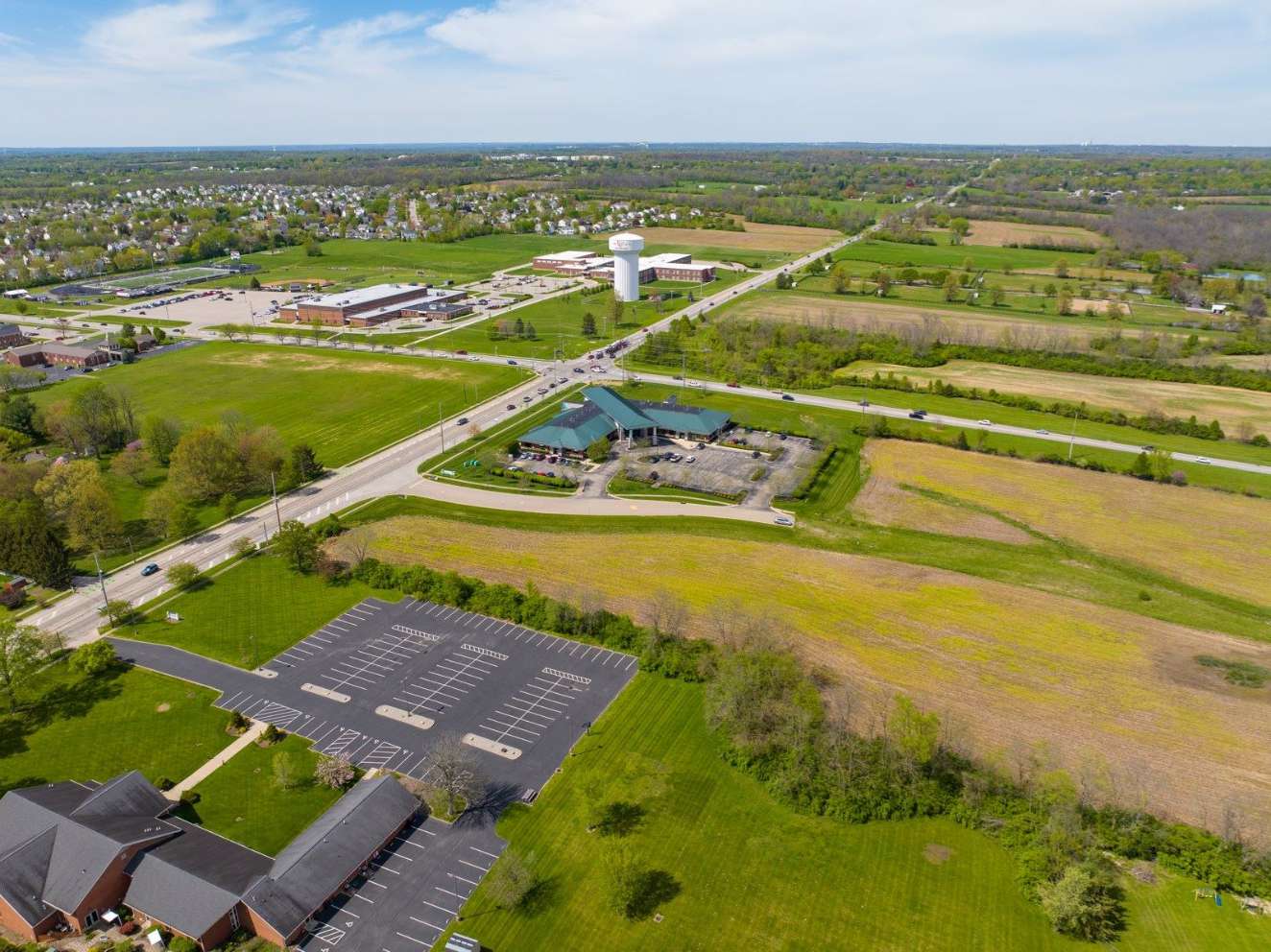 Aerial view of a commercial development with parking lot, buildings, and surrounding farmland and residential areas.
