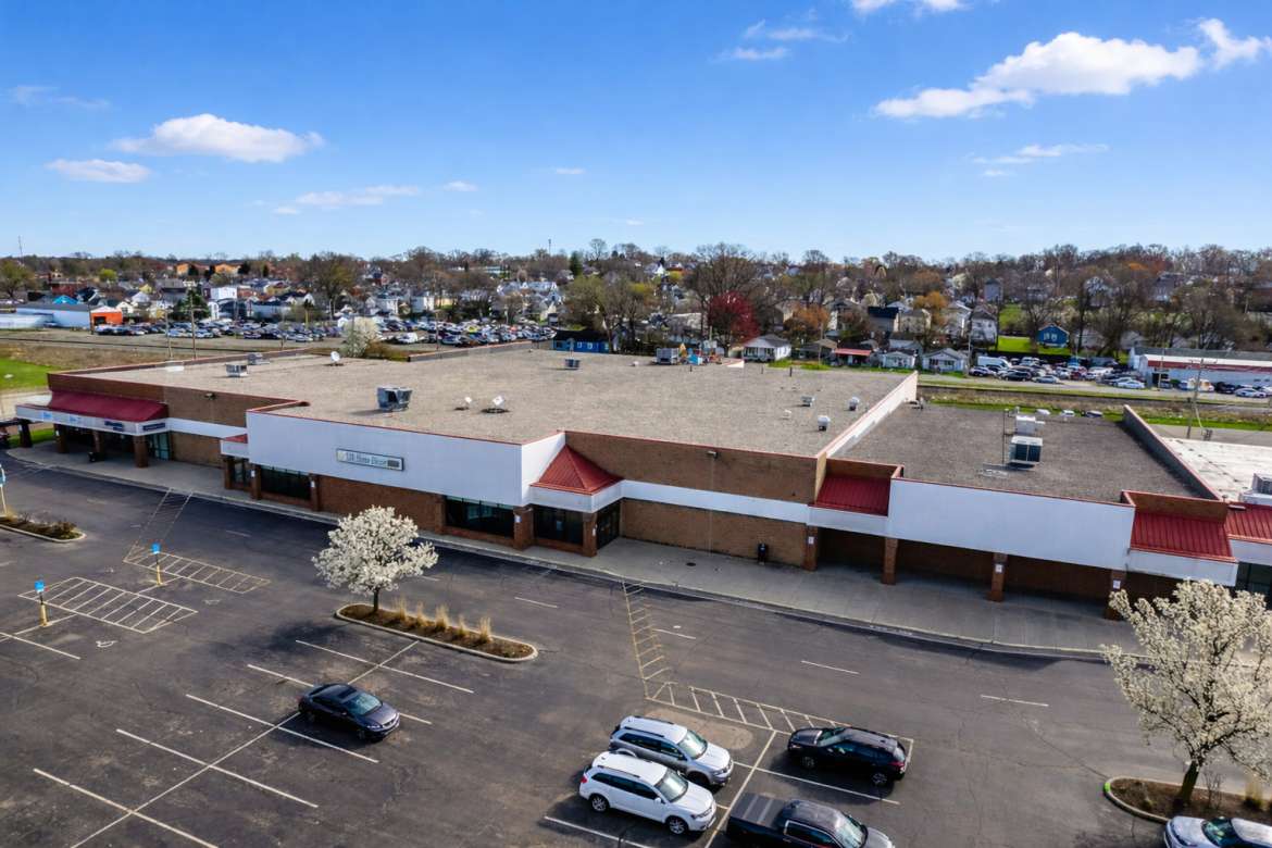 Aerial view of a commercial retail building with red and white exterior and large parking lot in a suburban area.