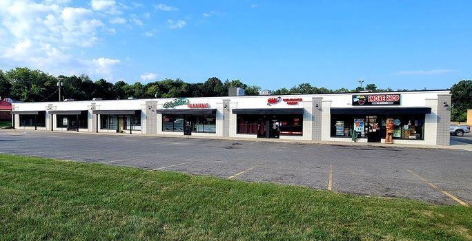 Modern single-story commercial strip mall with multiple storefronts and parking lot on a sunny day.