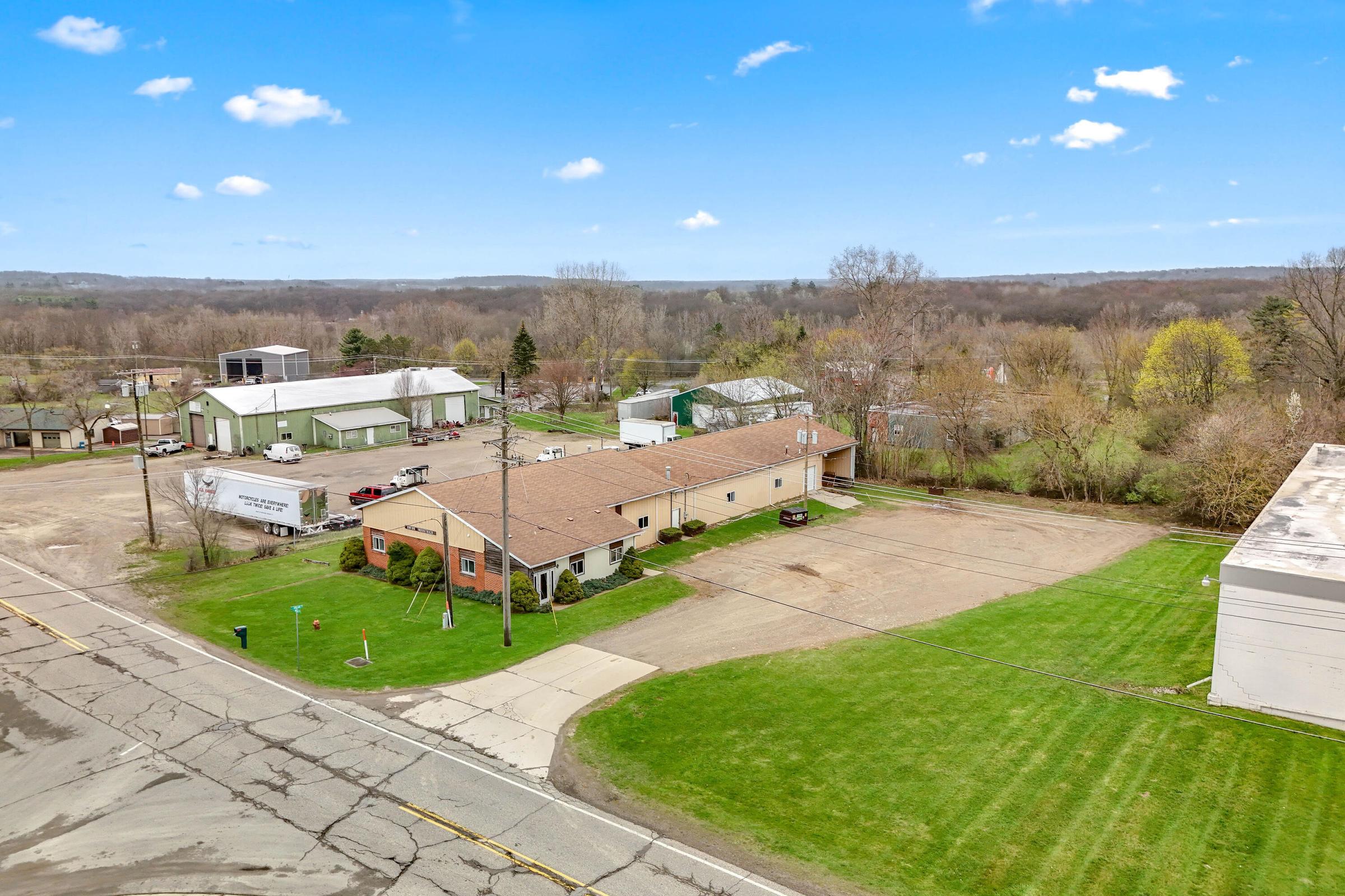 Aerial view of a brick commercial building with large paved lot and manicured lawn in a rural setting.