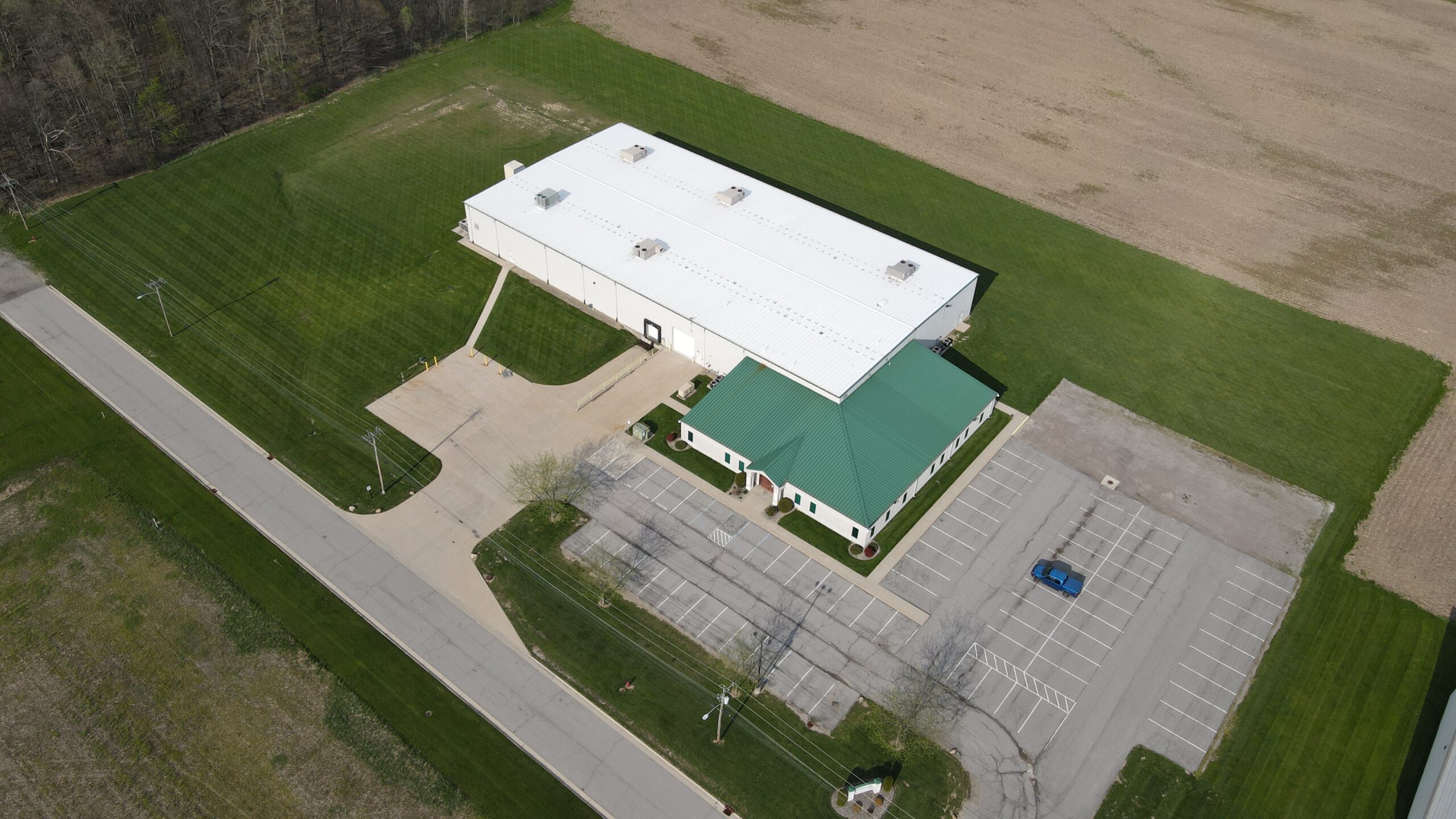 Aerial view of a commercial building with white roof, green structure, and solar panels in a rural setting.
