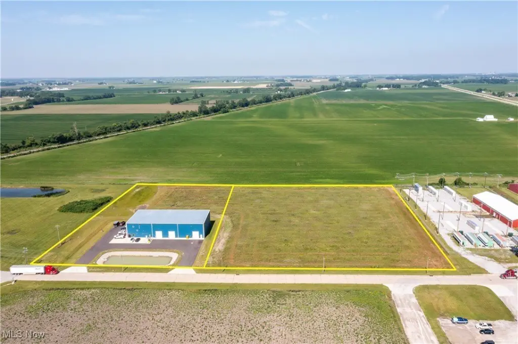 Aerial view of a rural industrial property with a blue warehouse building surrounded by green fields.