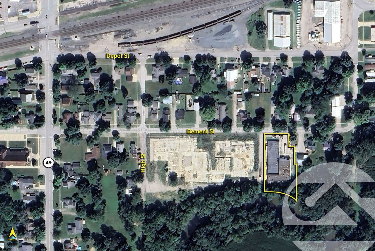 Aerial view of a residential neighborhood with a large cleared lot highlighted in yellow, surrounded by houses and trees.