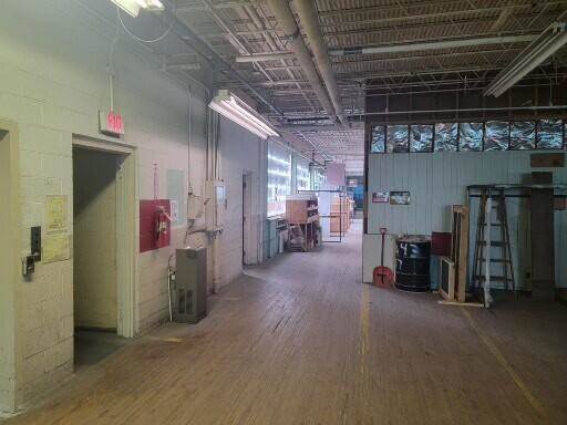 Spacious industrial warehouse interior with wooden floor, exposed ceiling, storage areas, and equipment along the sides.