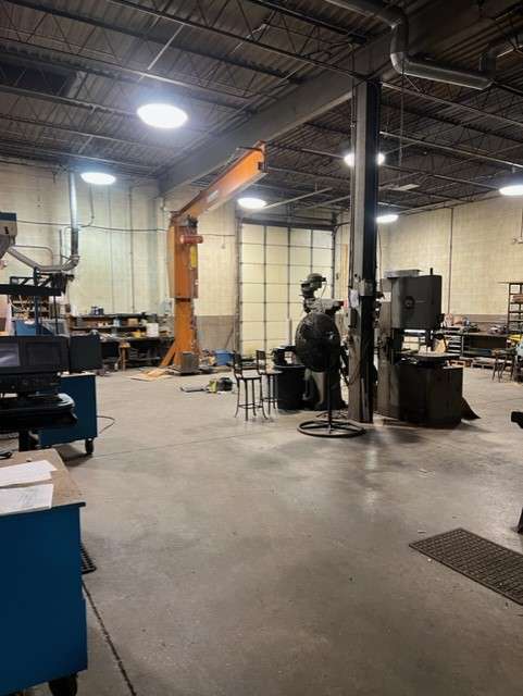 Industrial warehouse workspace with orange robotic arm and worker in safety gear at 444 Newell Street.