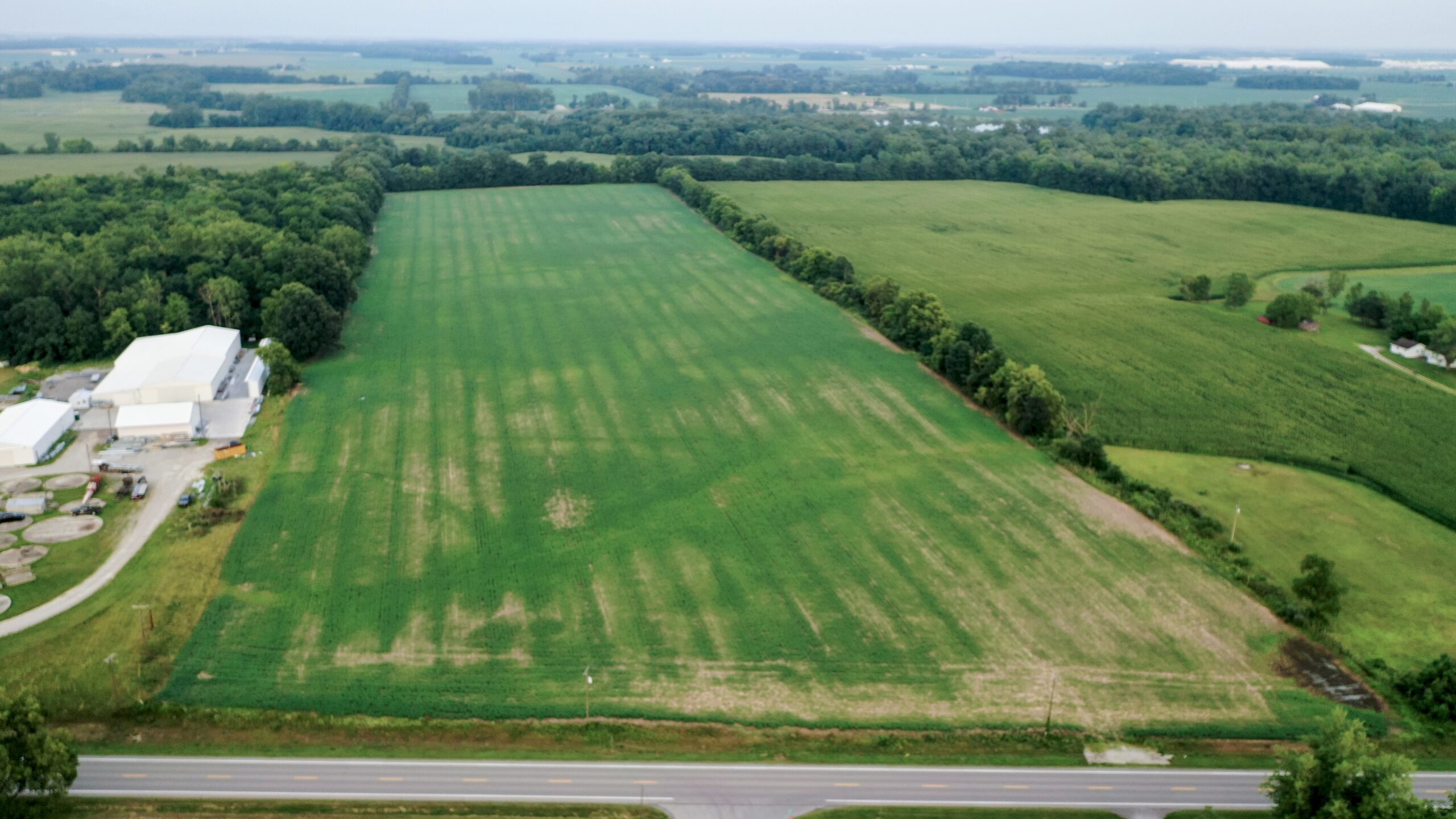 Aerial view of a large agricultural field with crop rows and surrounding farmland under clear skies.