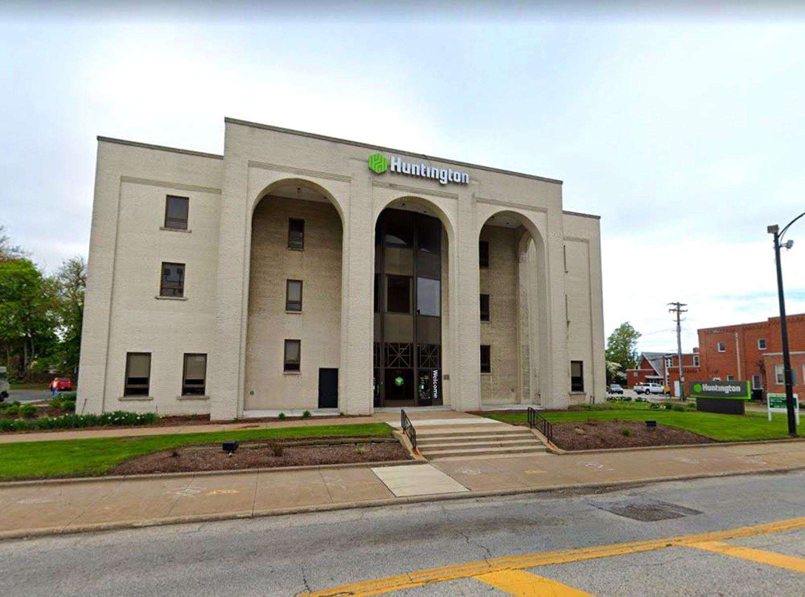 Huntington bank branch building with cream-colored facade and three large arches at the entrance on a tree-lined street.