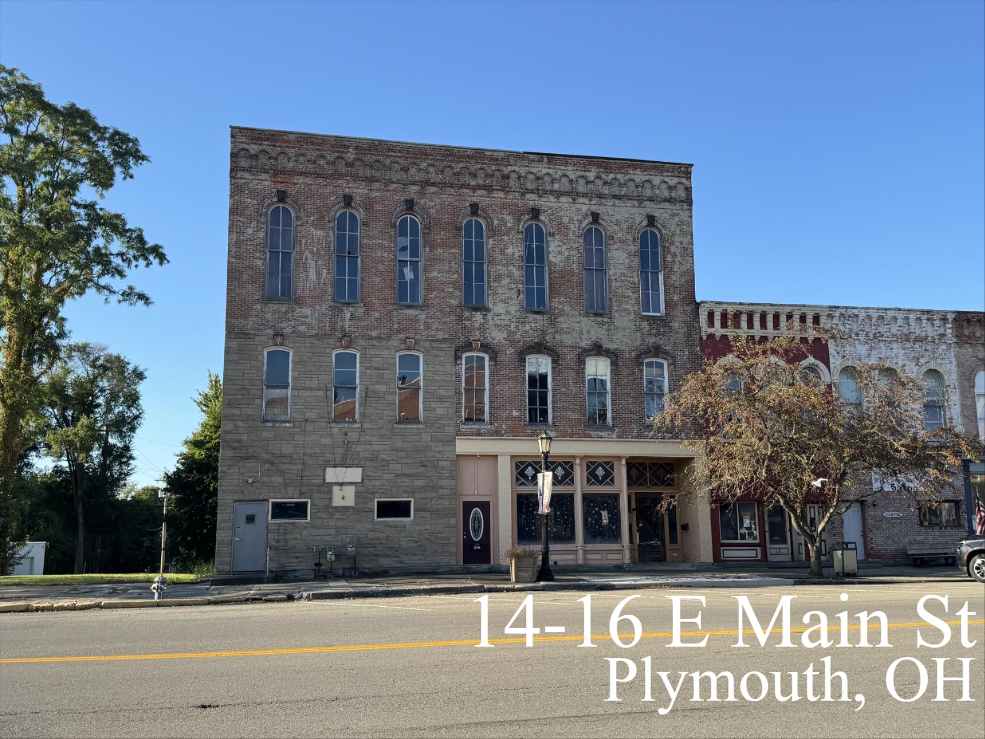 Historic brick buildings at 14-16 E Main St in Plymouth, Ohio with storefront windows and clear blue sky.