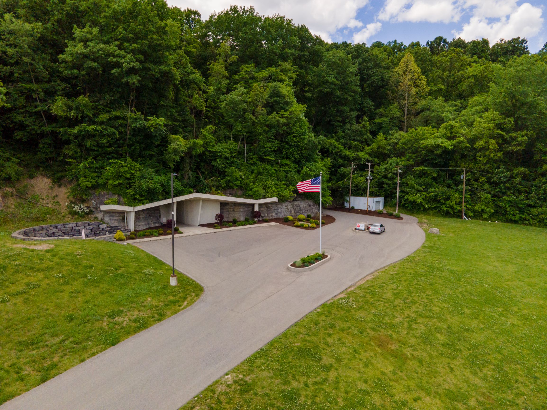 Aerial view of a modern building with parking area surrounded by green lawn and dense forest.