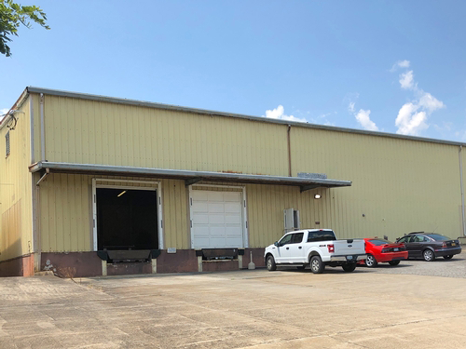 Industrial warehouse building with large garage doors and vehicles parked in front on a clear day.