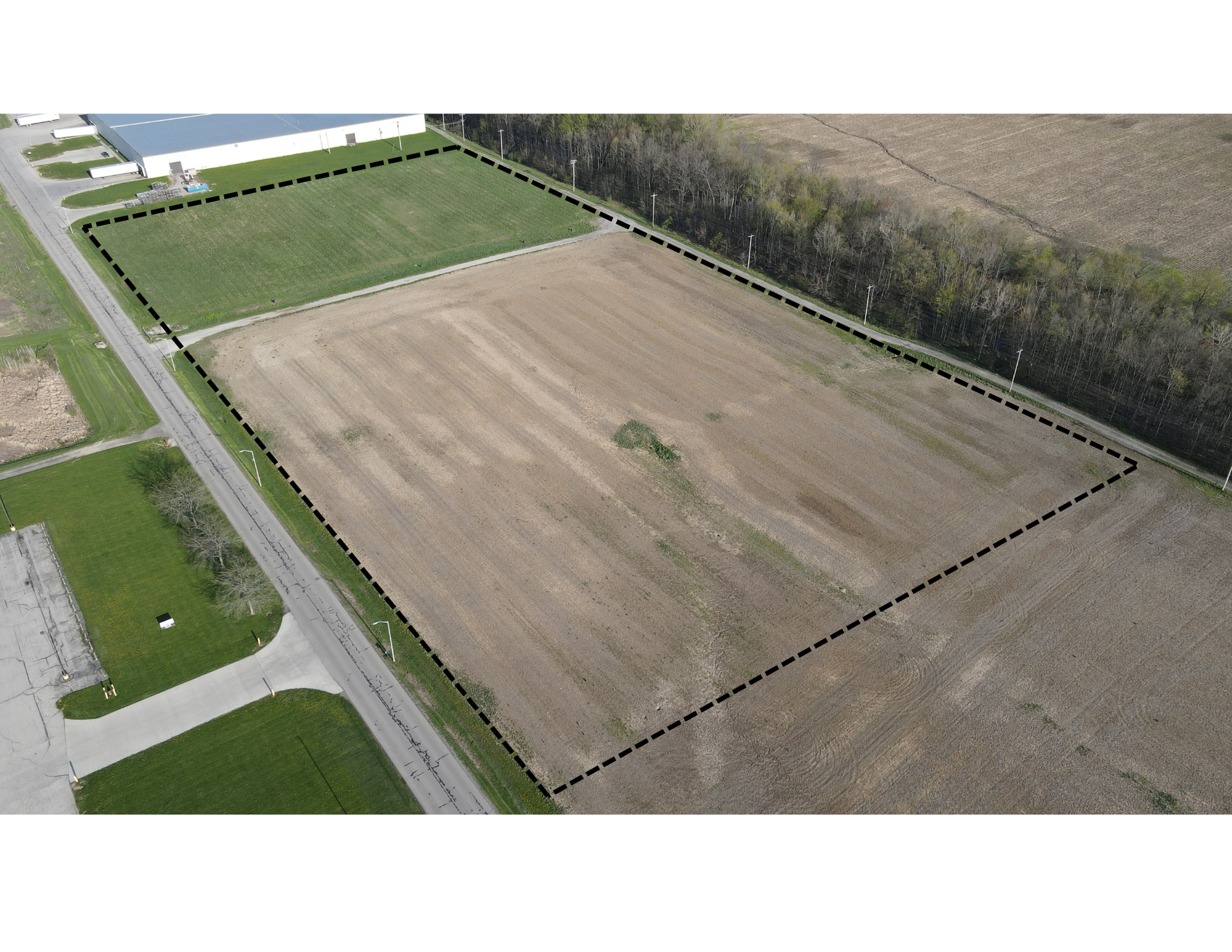 Aerial view of agricultural land with a green sports field and plowed field divided by tree lines.