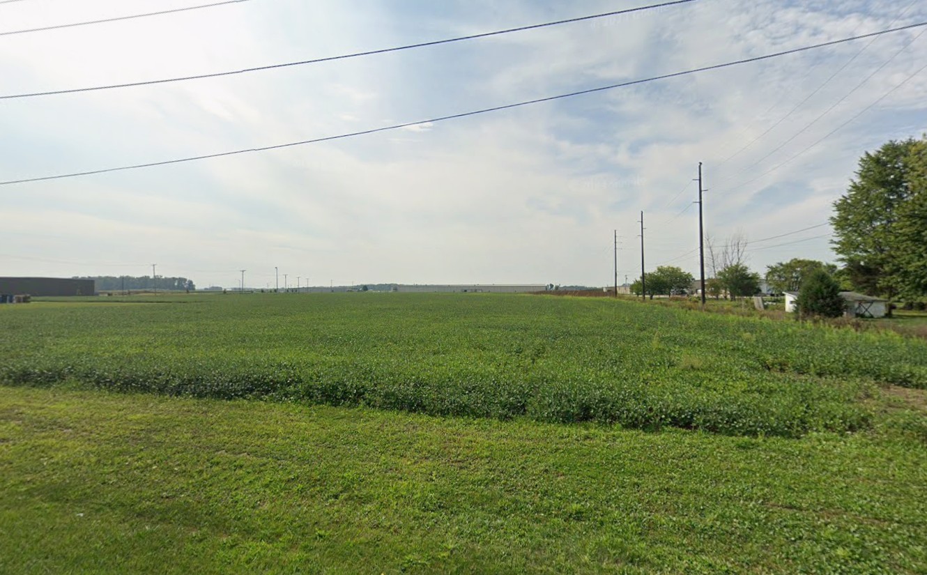 Wide agricultural field with rows of green crops and utility poles along a rural road.