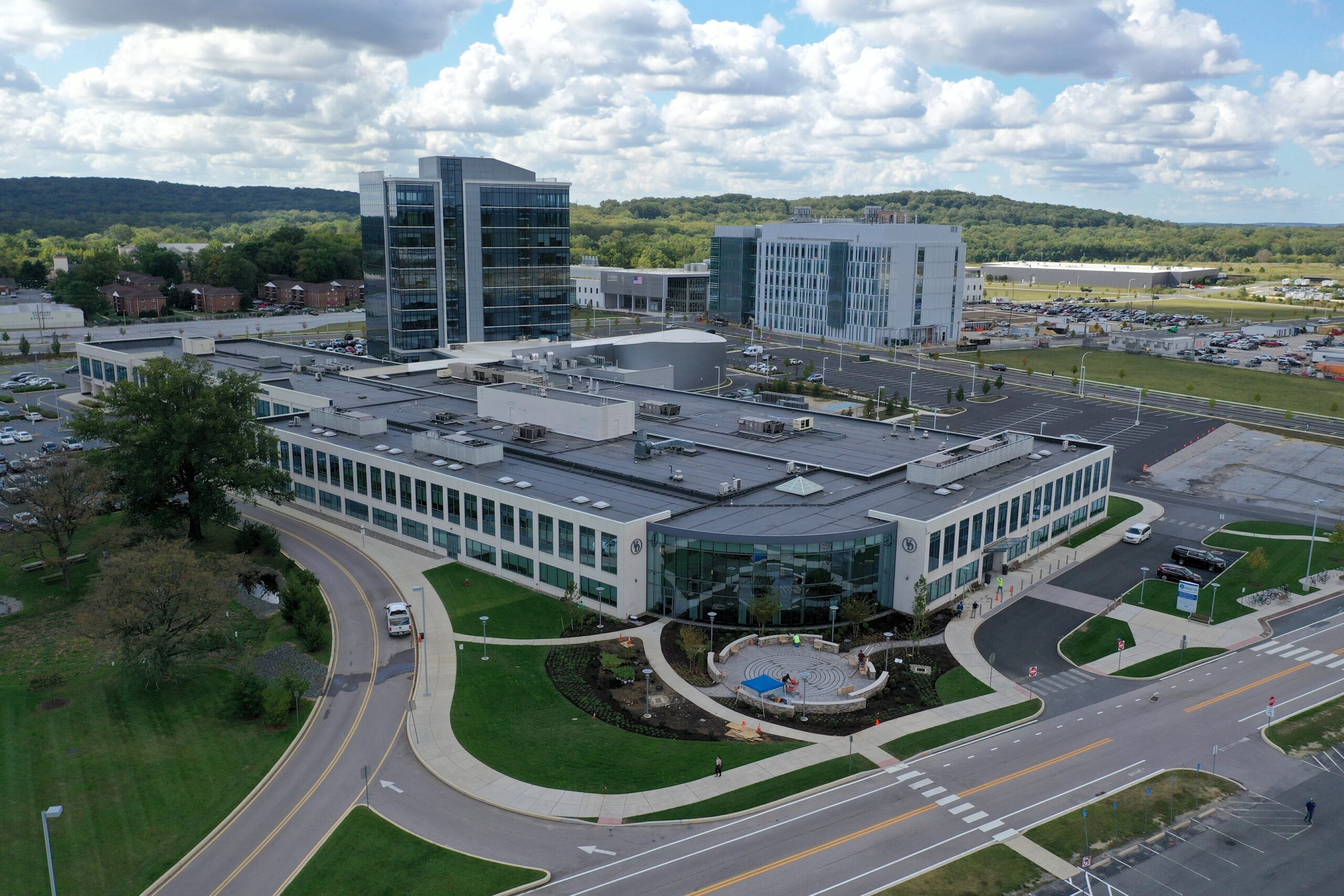 Aerial view of a modern commercial complex with curved architecture, green landscaping, and surrounding office buildings in a suburban setting.