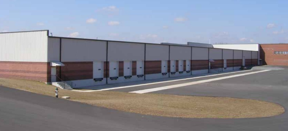 Modern industrial warehouse building with multiple loading dock doors and metal siding under clear sky.