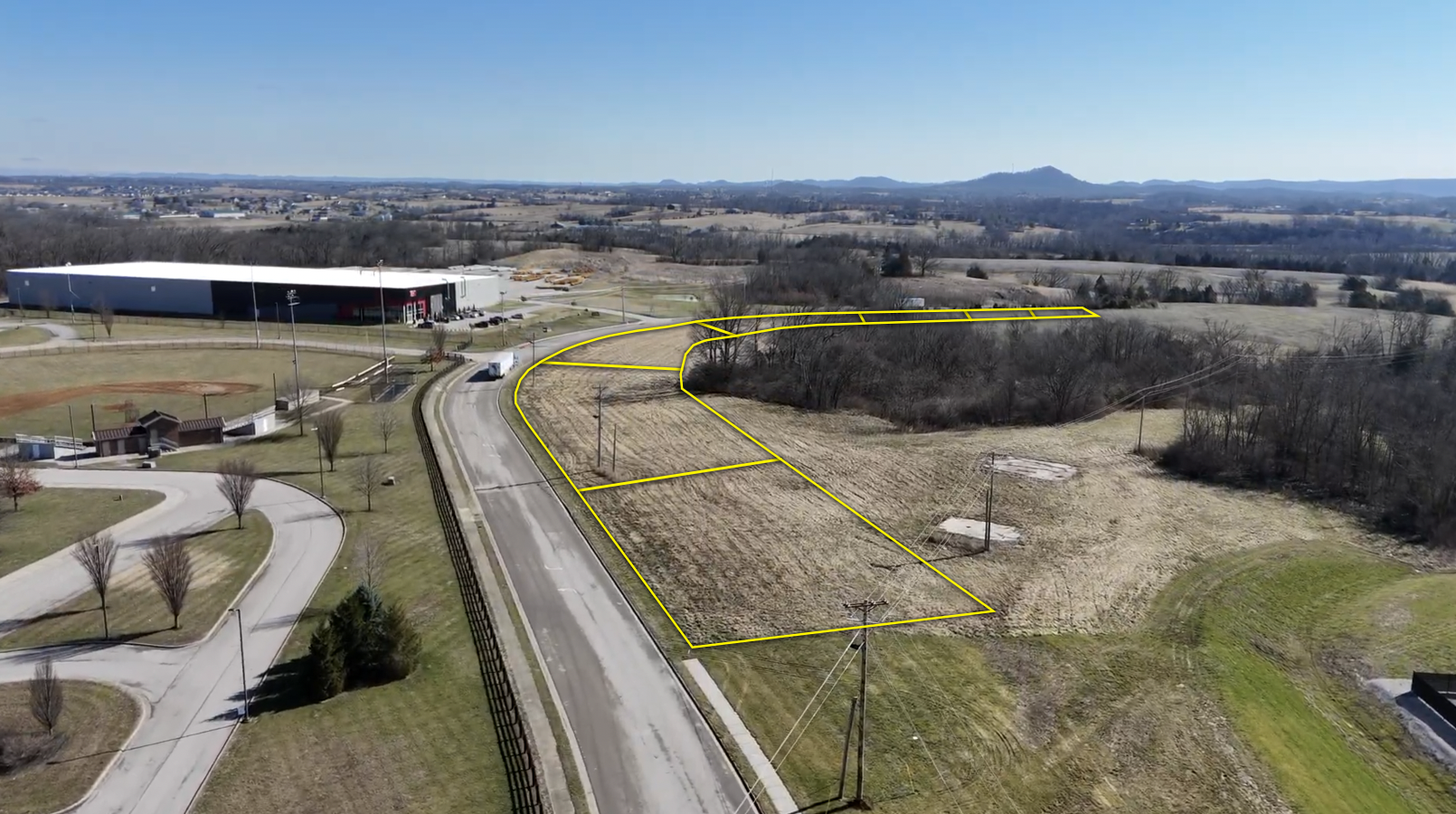 Aerial view of commercial property with large warehouse building, curved driveway, and outlined land parcels adjacent to a rural highway.