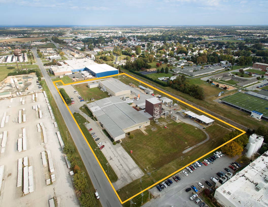Aerial view of an industrial property with yellow boundary lines, featuring warehouses and parking areas surrounded by residential neighborhoods.