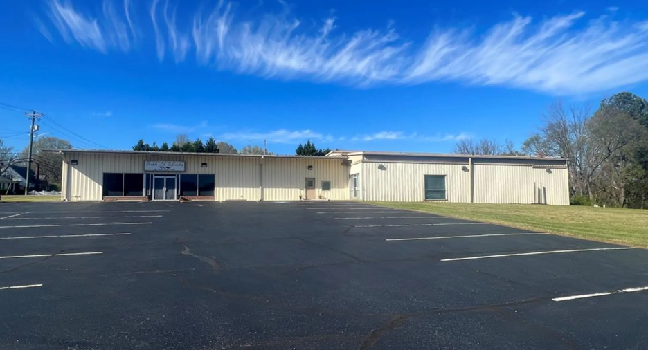 Single-story commercial metal building with parking lot on clear day with blue sky and scattered clouds.