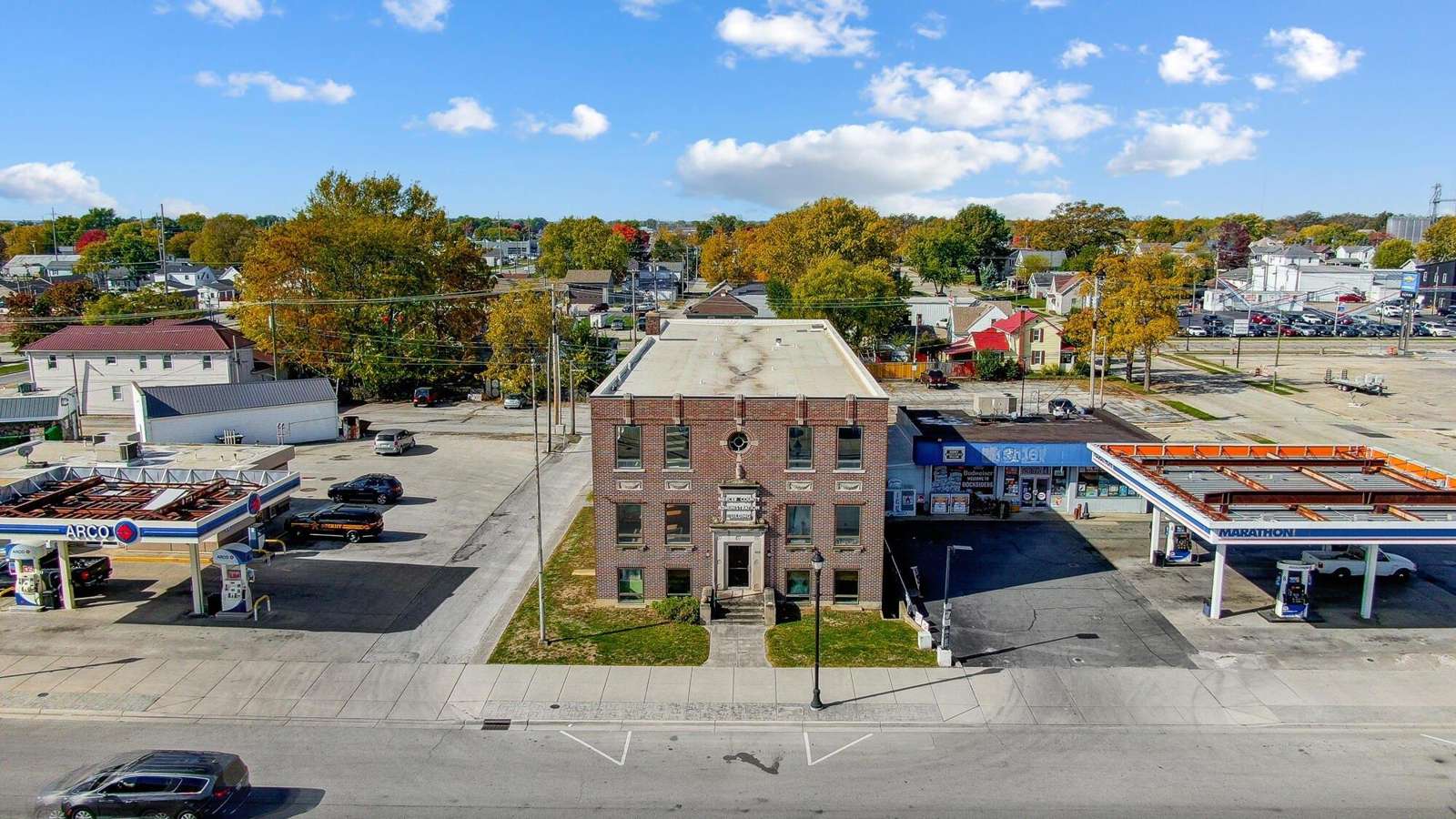 Aerial view of a historic brick building surrounded by commercial structures and residential neighborhoods on a sunny day.