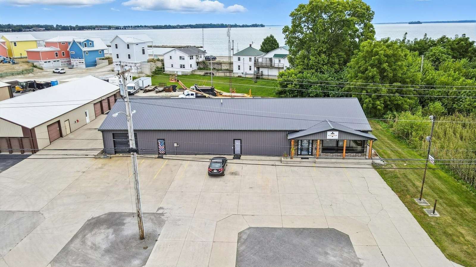 Aerial view of a commercial building with dark roof and parking area, surrounded by residential homes and green landscape.