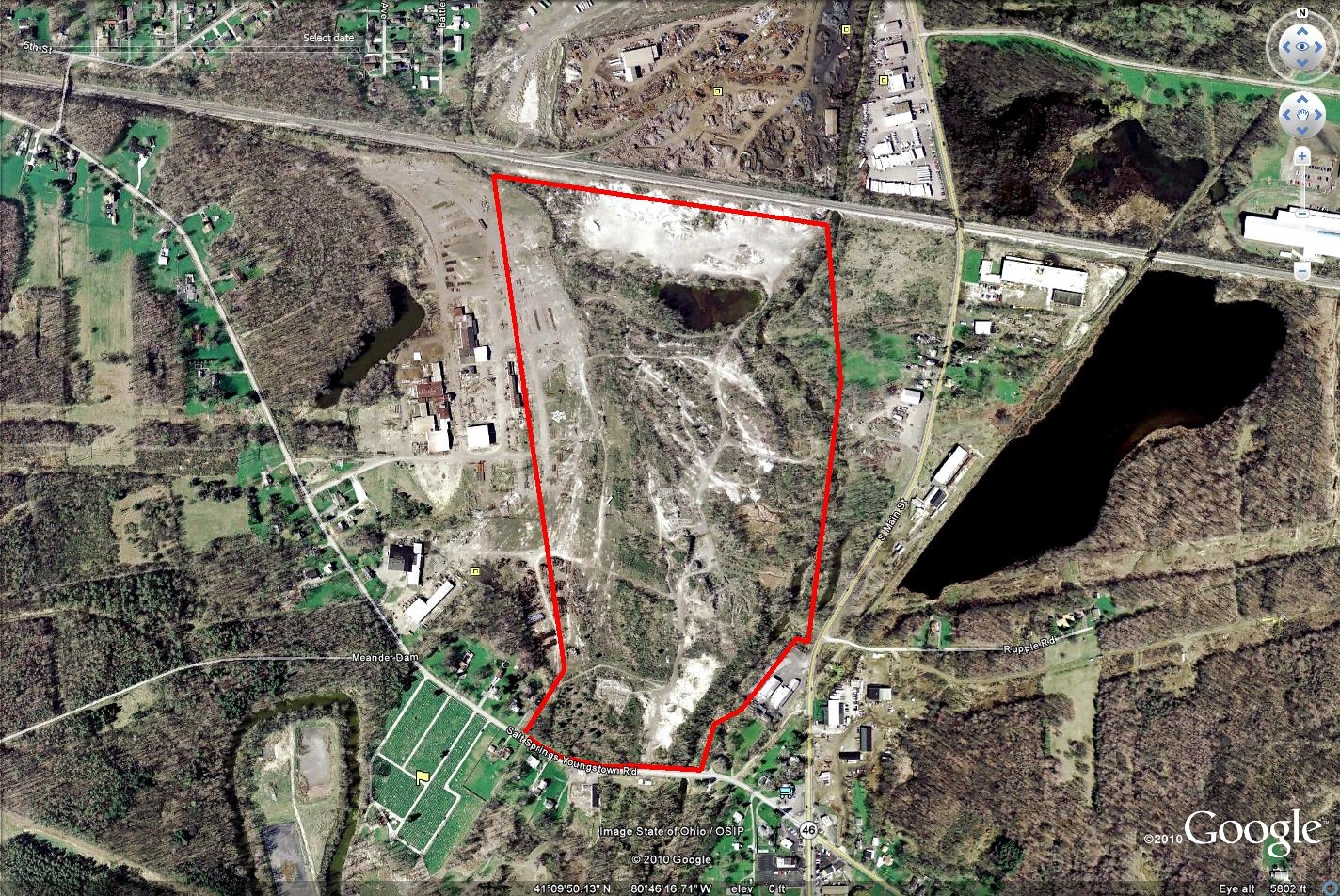 Aerial satellite view of a quarry or mining site outlined in red, surrounded by forested areas and adjacent facilities.
