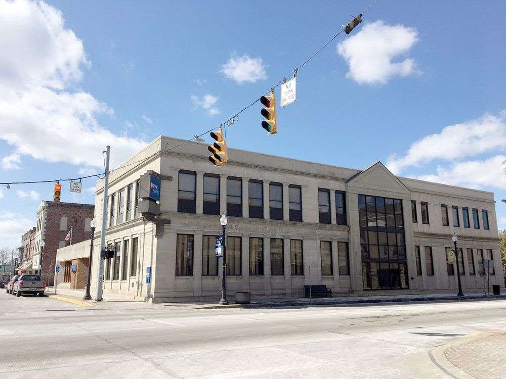PNC Bank building, a historic beige stone structure with large windows on a city street corner under blue sky.