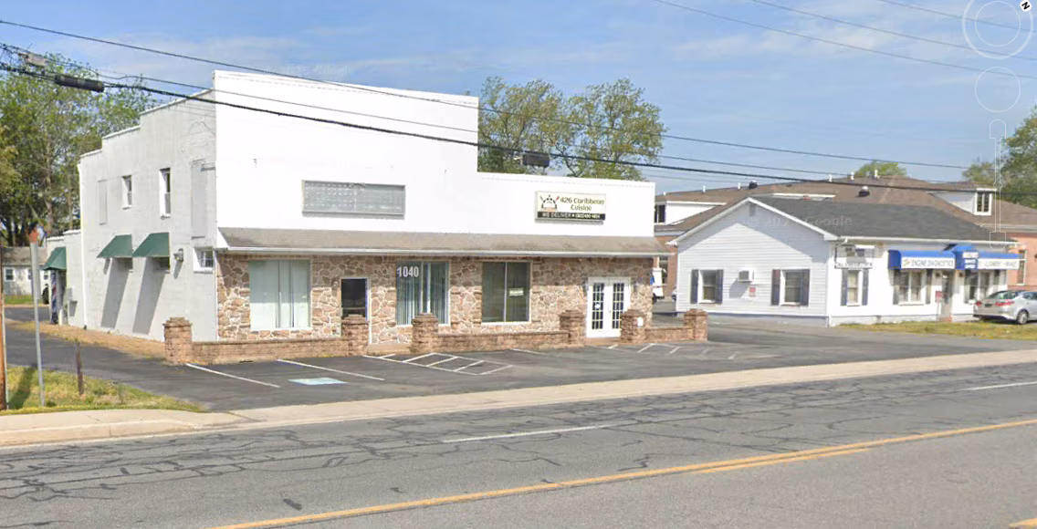 A modern white commercial building with stone base next to a traditional white house with blue storefront on a street corner.