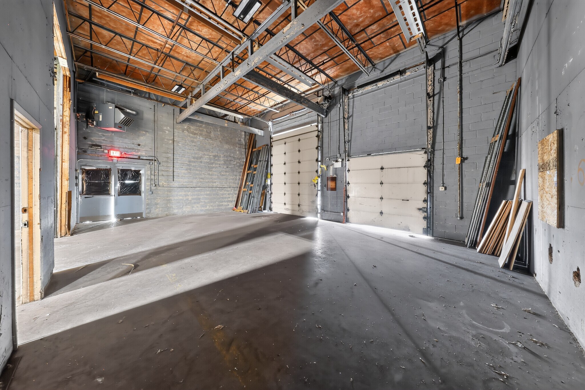 Empty garage interior with open door, concrete floor, white walls, and exposed ceiling framing.