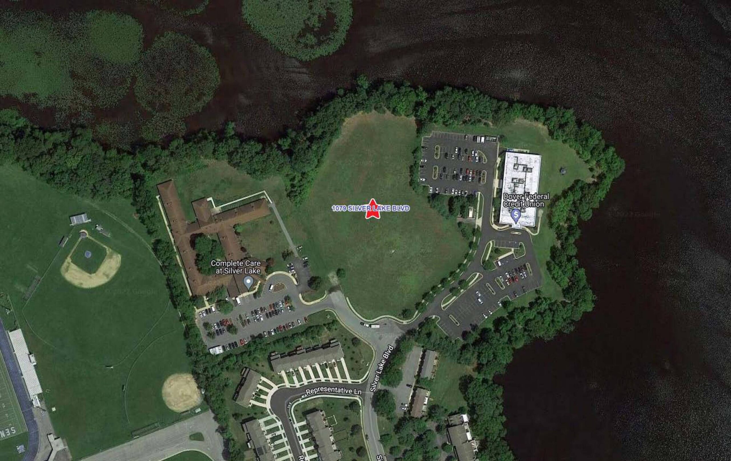 Aerial view of a waterfront institution with athletic fields, parking areas, and surrounding green space.
