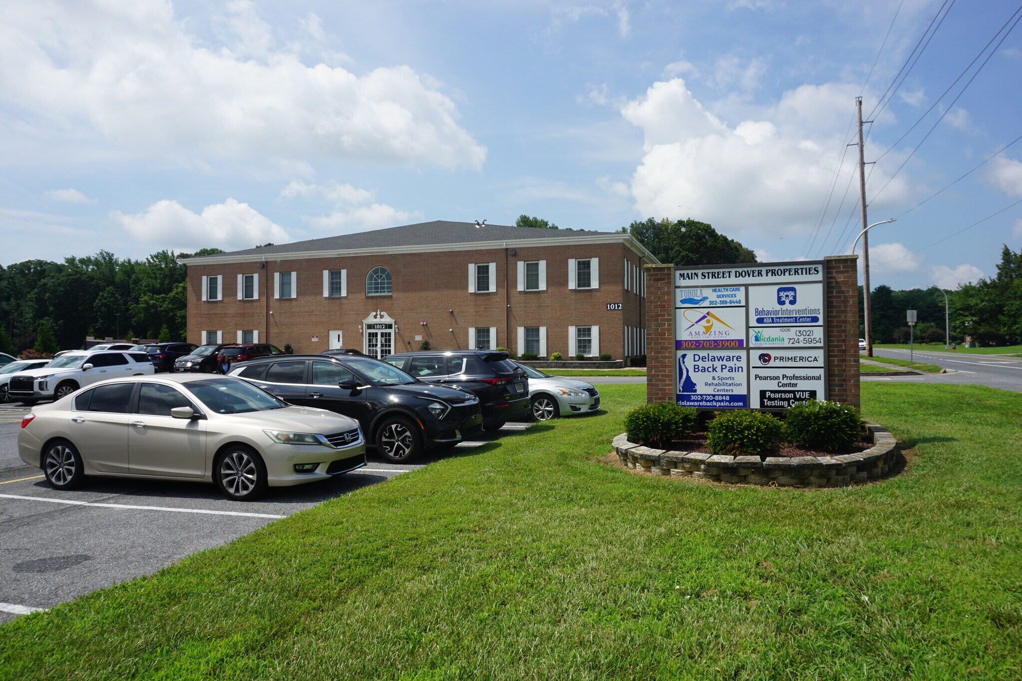 Brick professional office building with parked cars and directional signage on a sunny day.