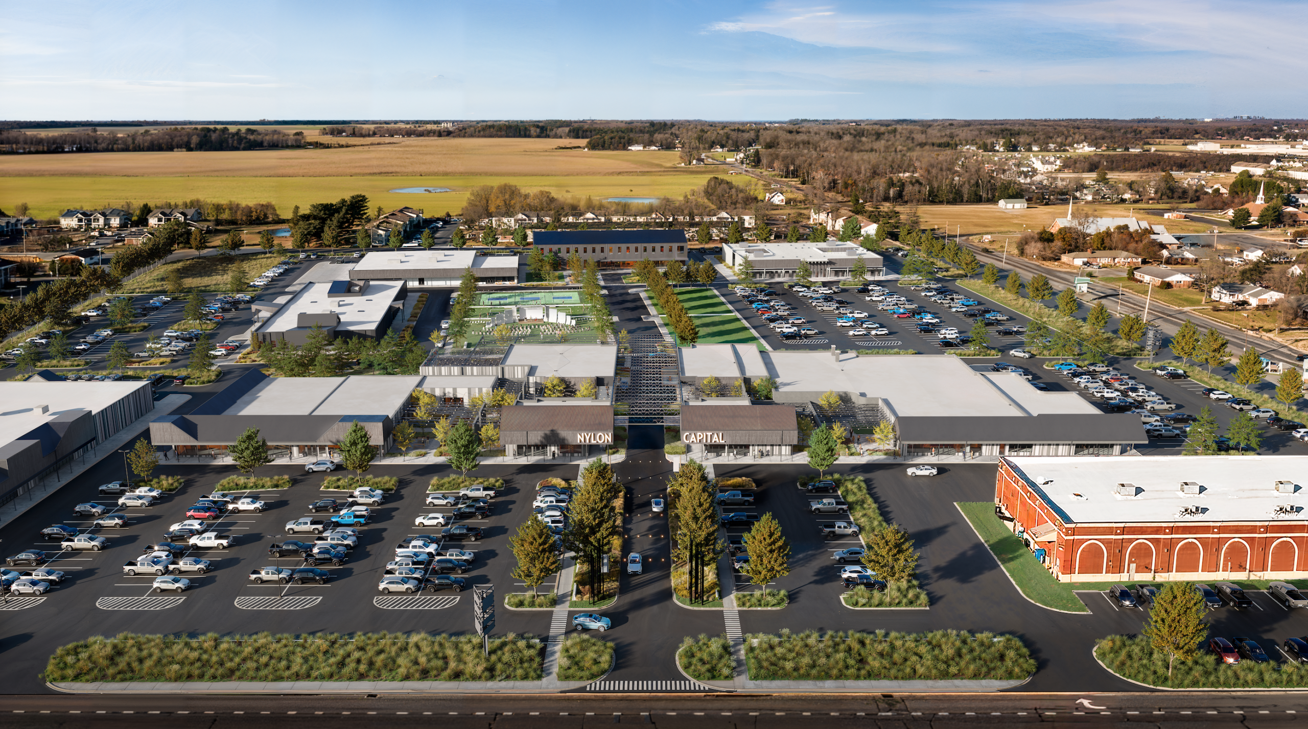 Aerial view of a modern retail and commercial shopping center with parking lots and green landscaping in a rural area.