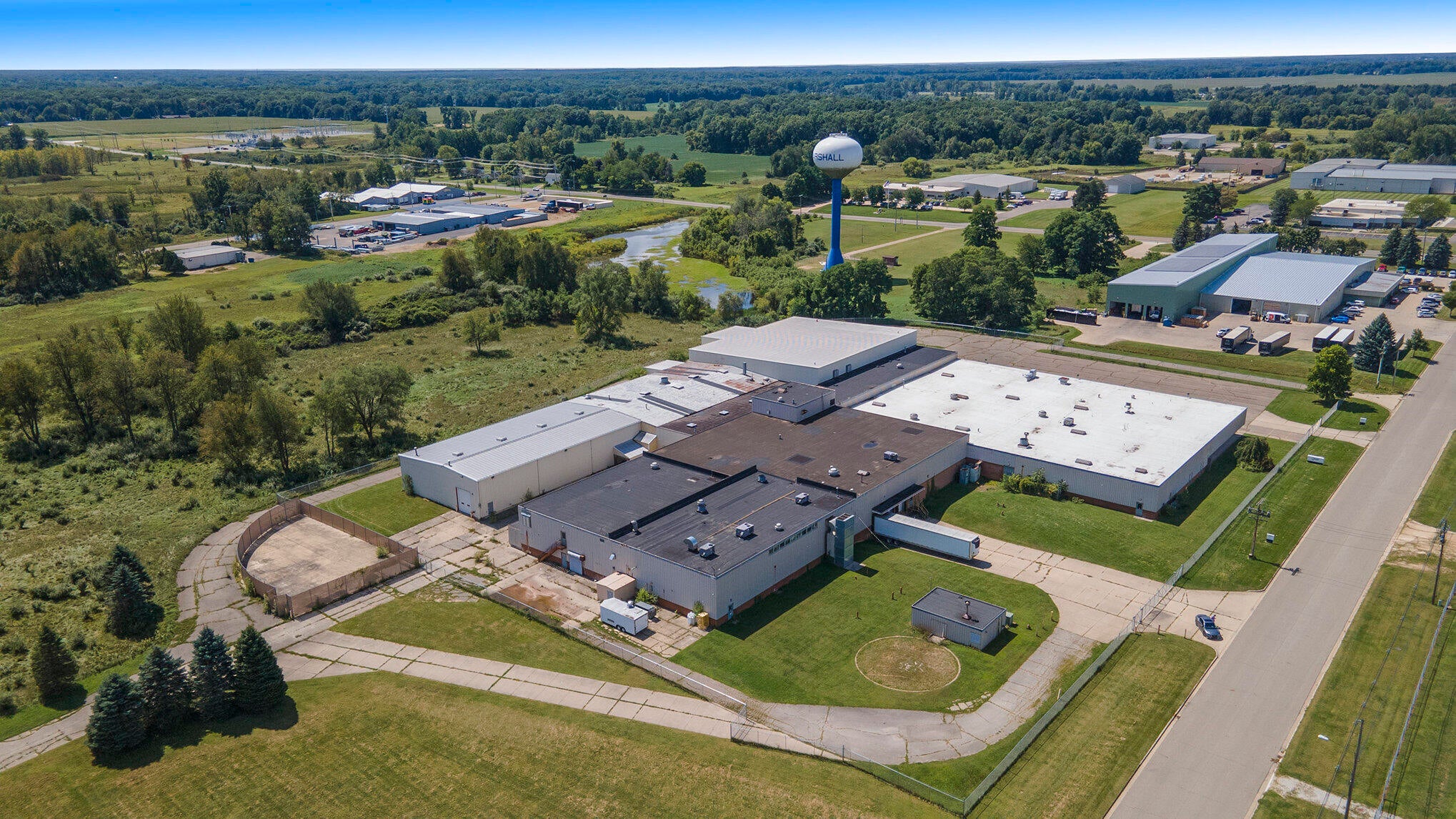 Aerial view of a large industrial manufacturing facility with white roofed buildings surrounded by green fields and rural landscape.