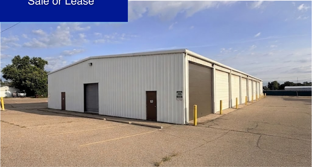 Modern industrial warehouse with metal siding and large bay doors on a paved lot under clear sky.
