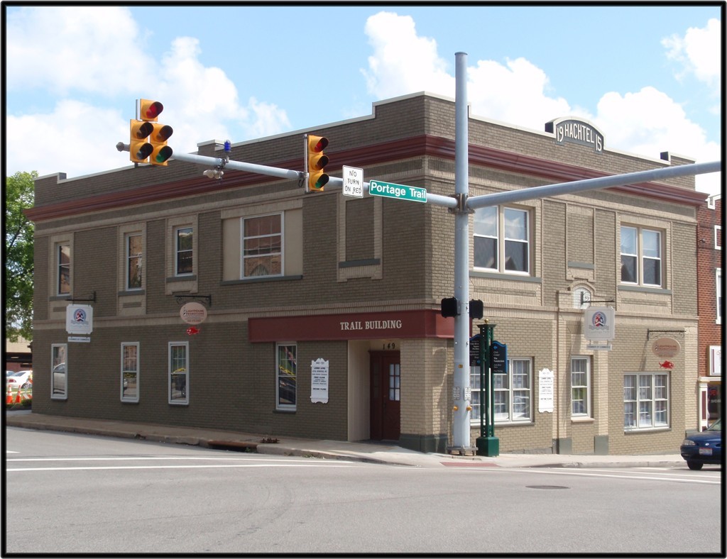 Corner brick building with storefronts at an urban intersection with traffic light overhead.